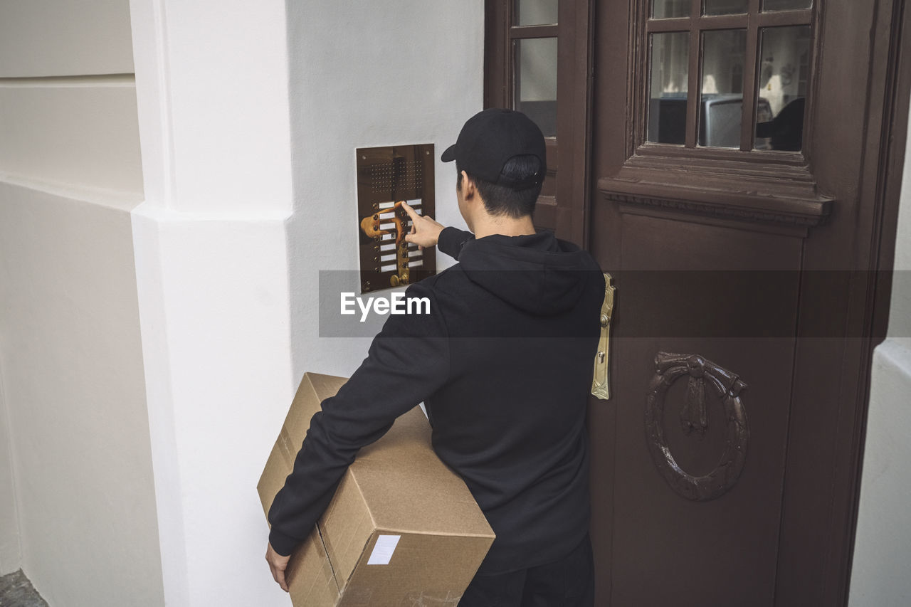 Rear view of delivery man ringing bell at doorstep