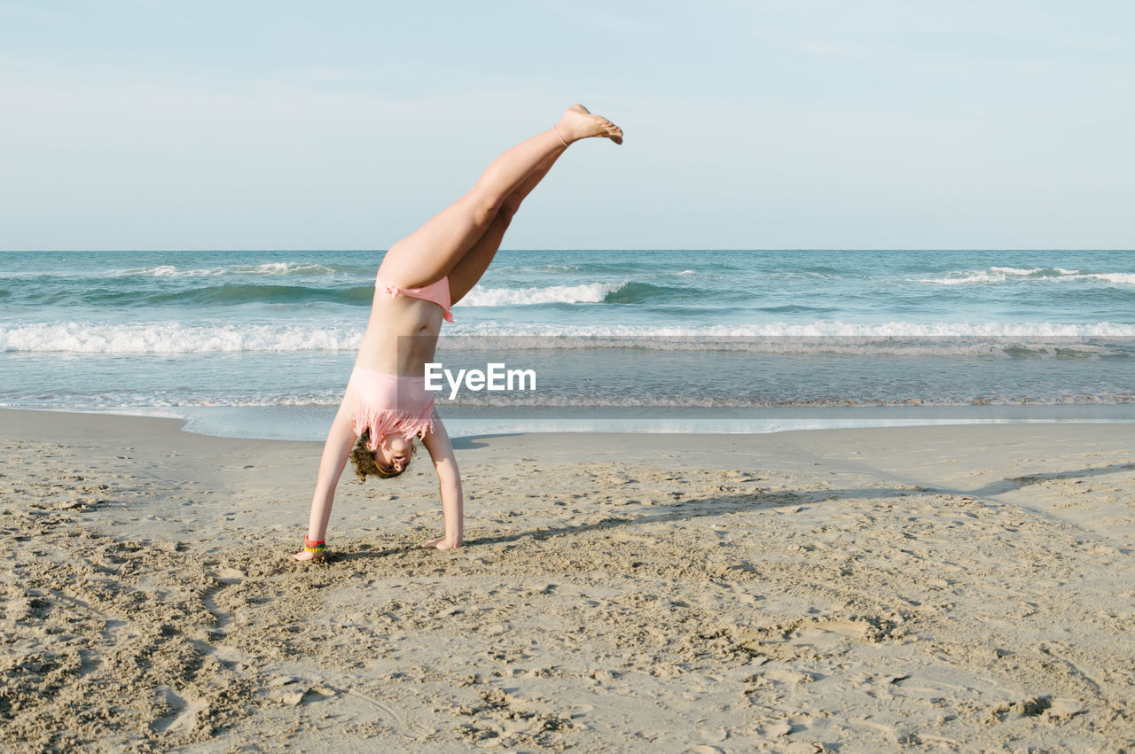 Teenager performing cartwheel at beach against sky