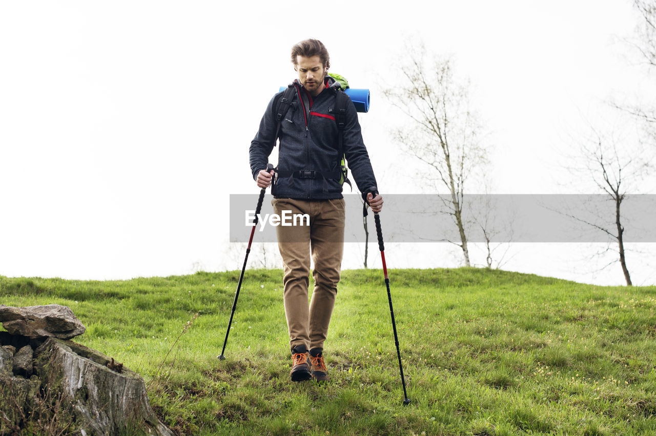 Full length of male hiker walking on mountain against clear sky