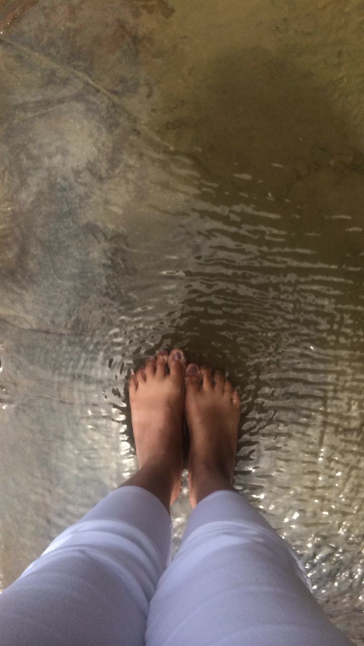 LOW SECTION OF WOMAN STANDING IN WATER AT THE EDGE