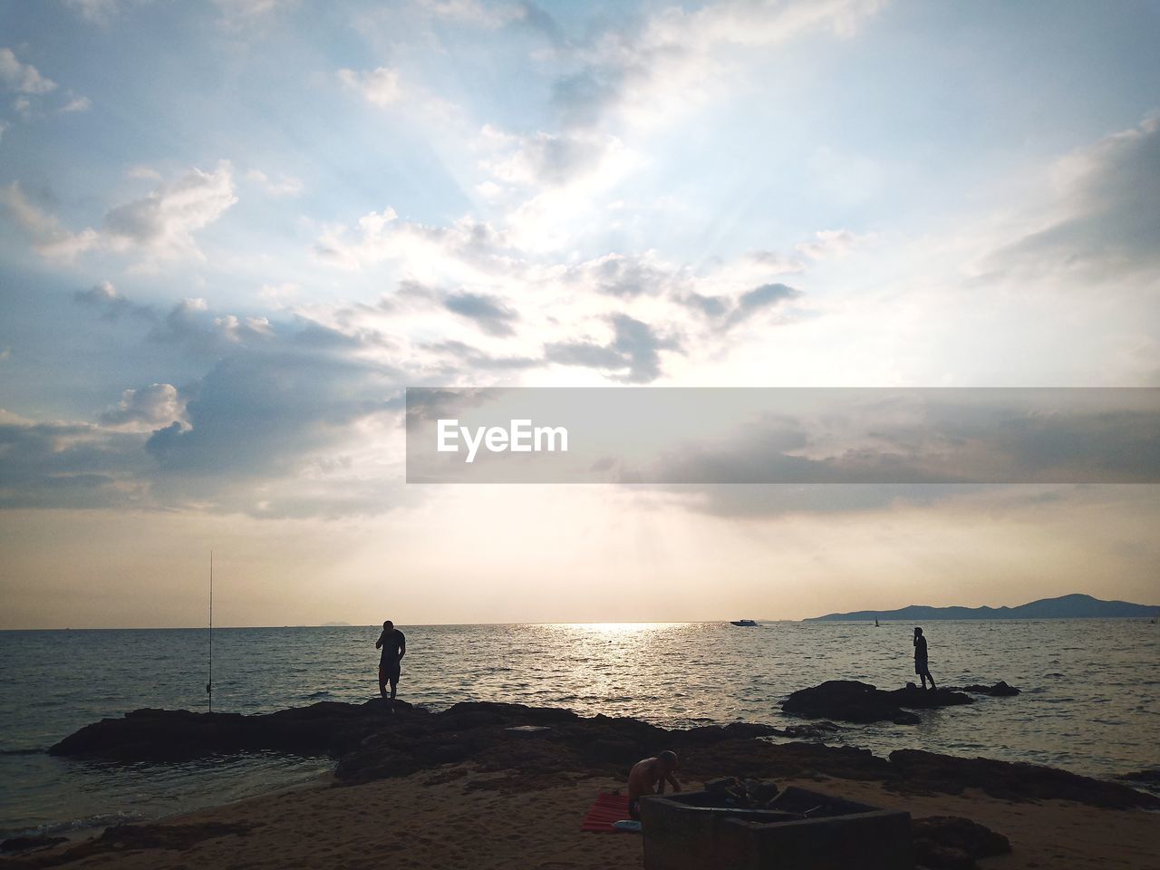 Men standing on rock by sea during sunset