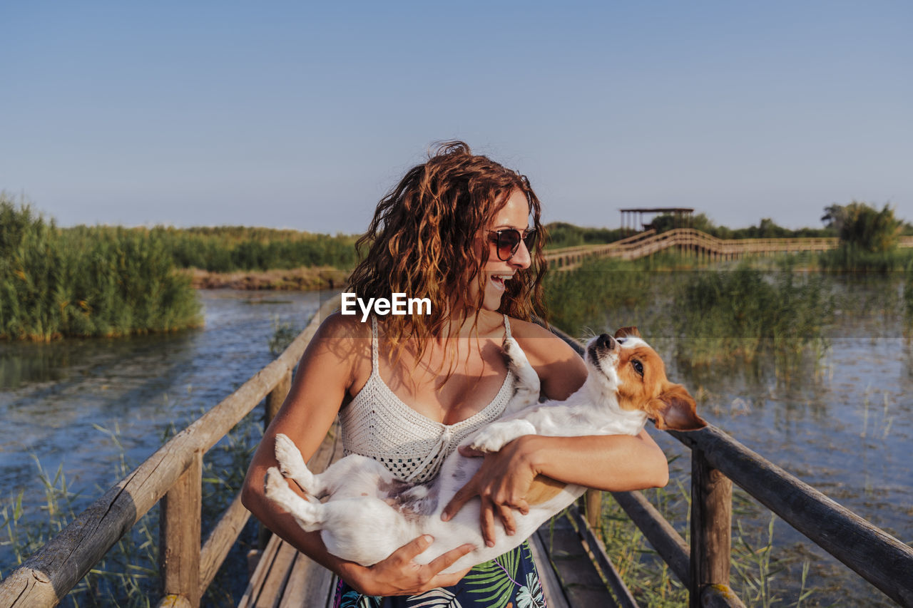 Smiling woman with dog on footbridge against sky