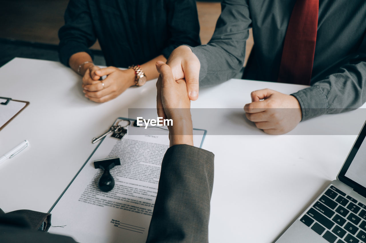 Business colleagues shaking hands at desk in office