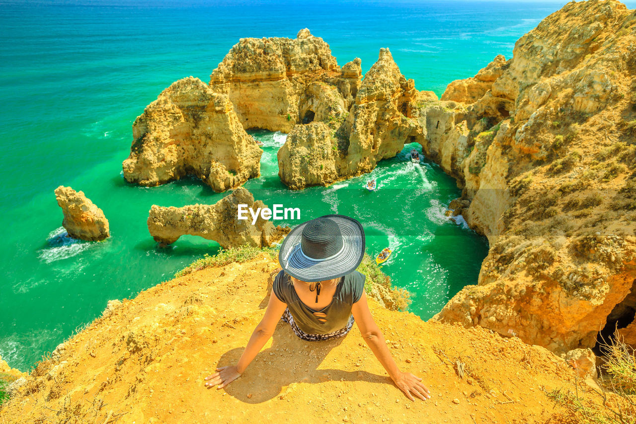 Rear view of woman sitting on cliff against sea