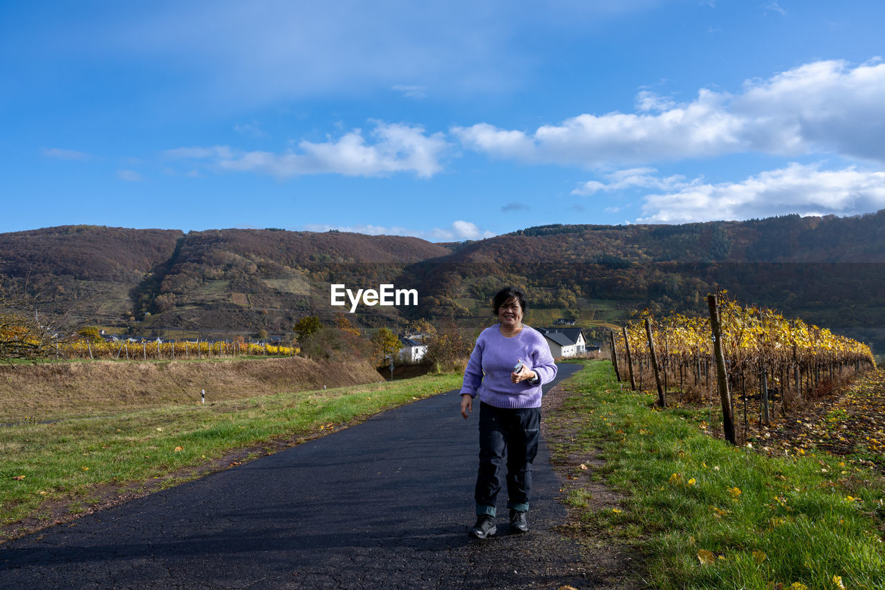 MAN STANDING ON ROAD AGAINST MOUNTAIN