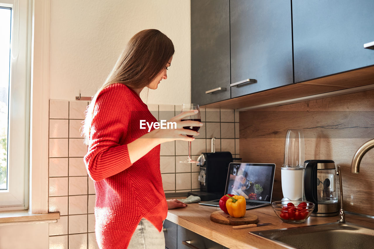 A young woman prepares a salad in the kitchen online and drinks red wine. cooking courses online