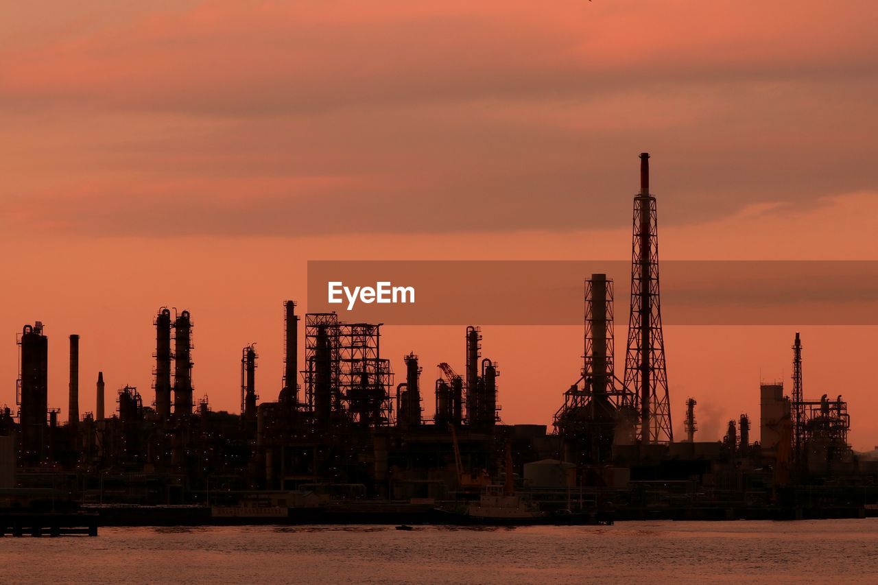 Cranes by sea against sky during sunset