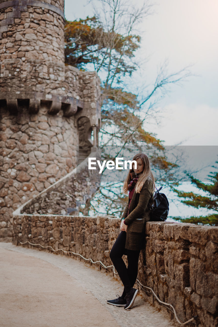 Full length of woman standing by retaining wall against trees and sky