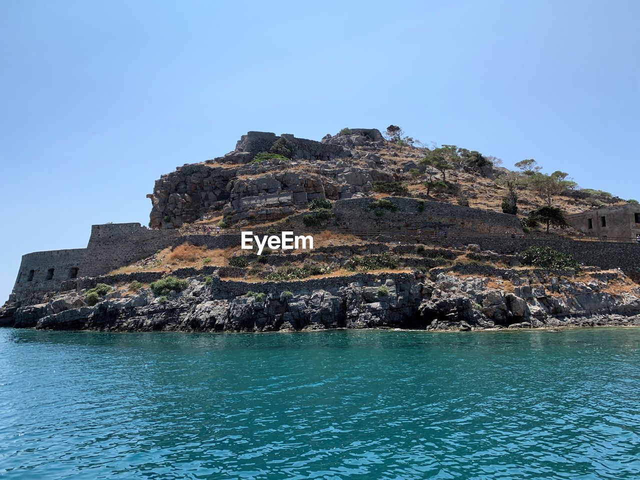 Sea by rocks against clear blue sky