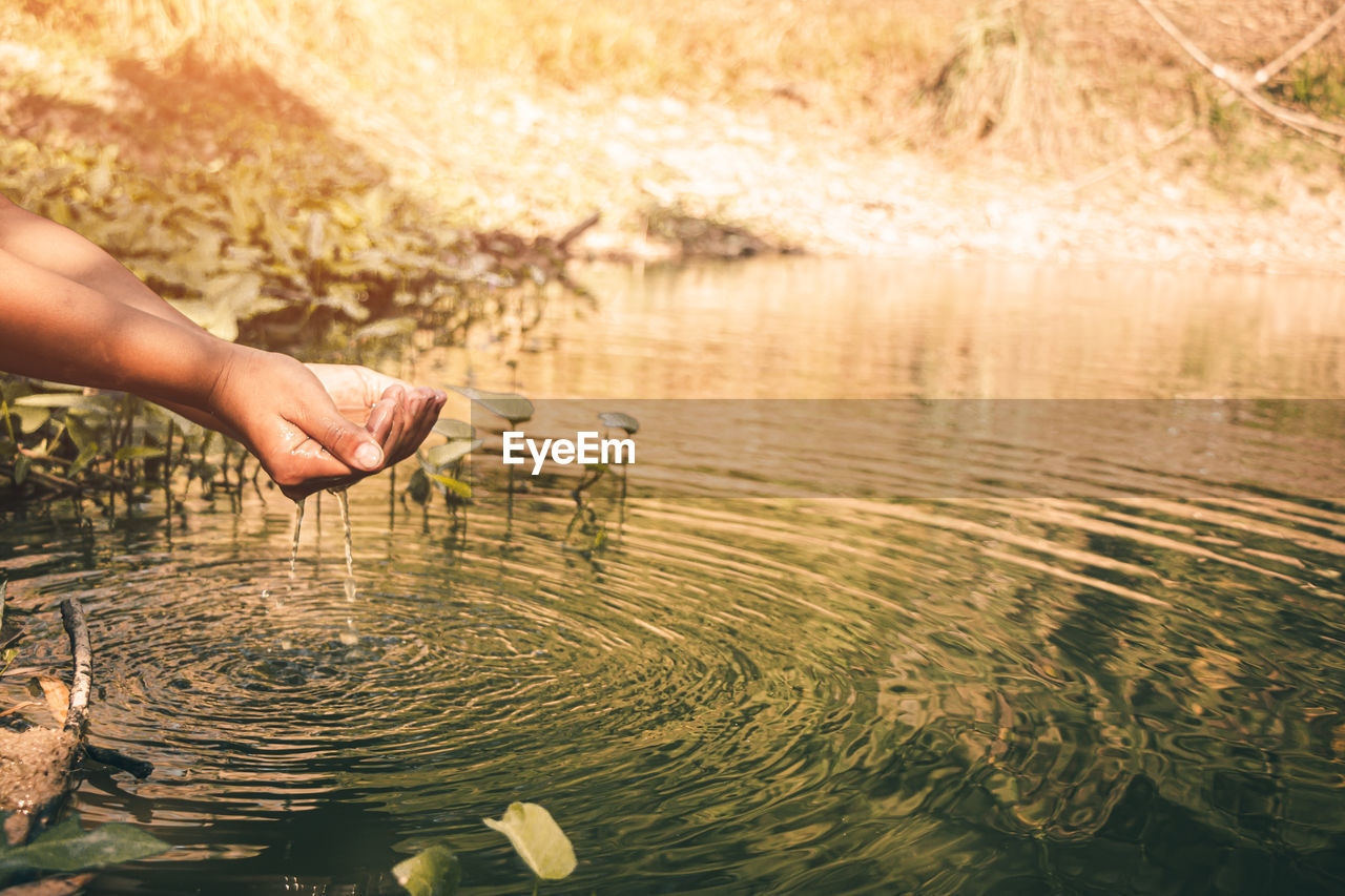 Midsection of man touching water in lake