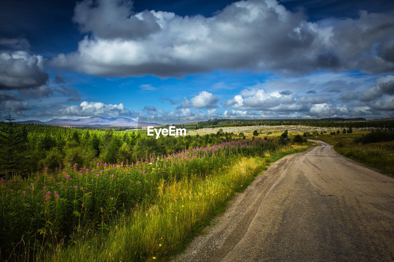 ROAD PASSING THROUGH FIELD AGAINST CLOUDY SKY