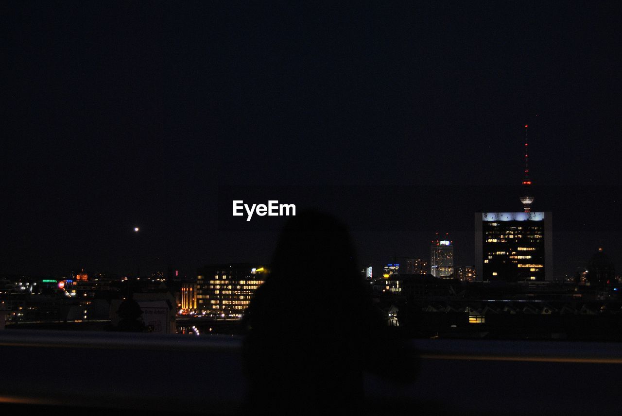 REAR VIEW OF SILHOUETTE MAN AGAINST ILLUMINATED CITYSCAPE