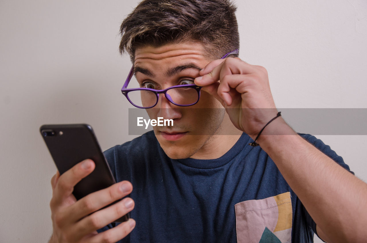 PORTRAIT OF YOUNG MAN USING SMART PHONE OUTDOORS