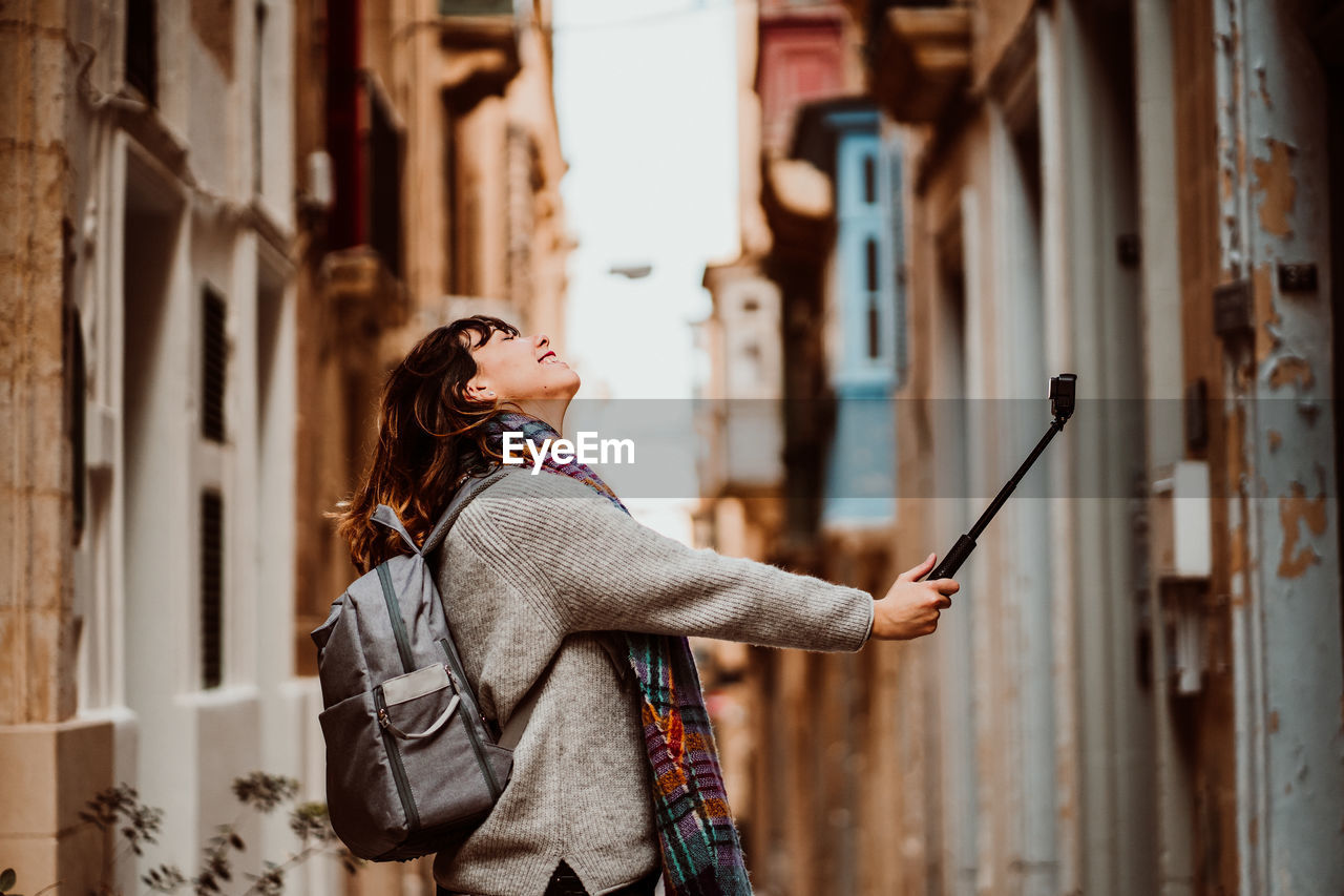 Side view of woman holding monopod standing in alley