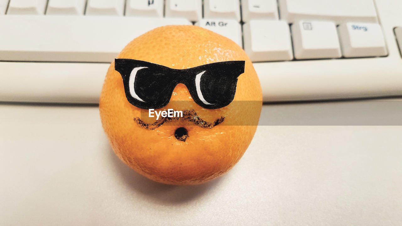 Close-up of anthropomorphic face on orange fruit at desktop
