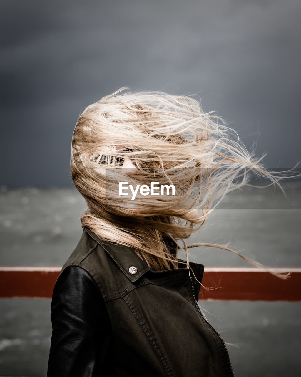 Woman with obscured face standing by railing against cloudy sky