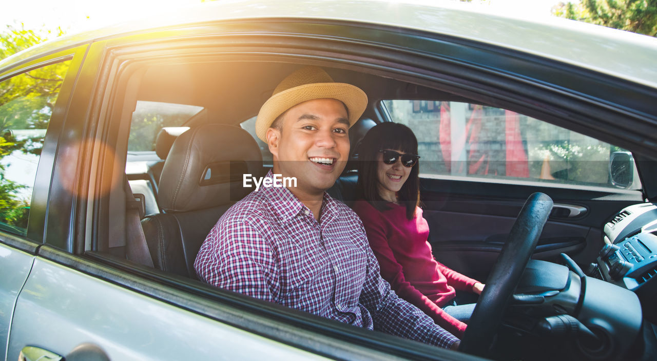 PORTRAIT OF SMILING MAN SITTING ON CAR