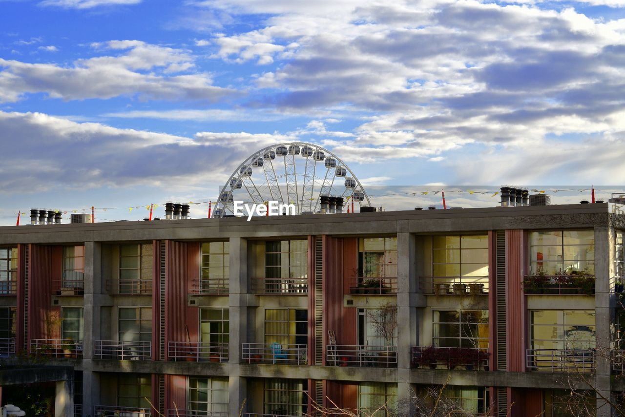 Ferris wheel in city against cloudy sky