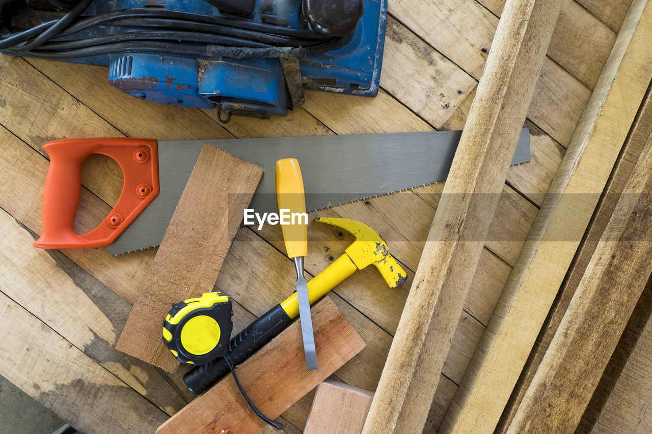 Directly above shot of hammer with hand saw and tape measure on wooden plank