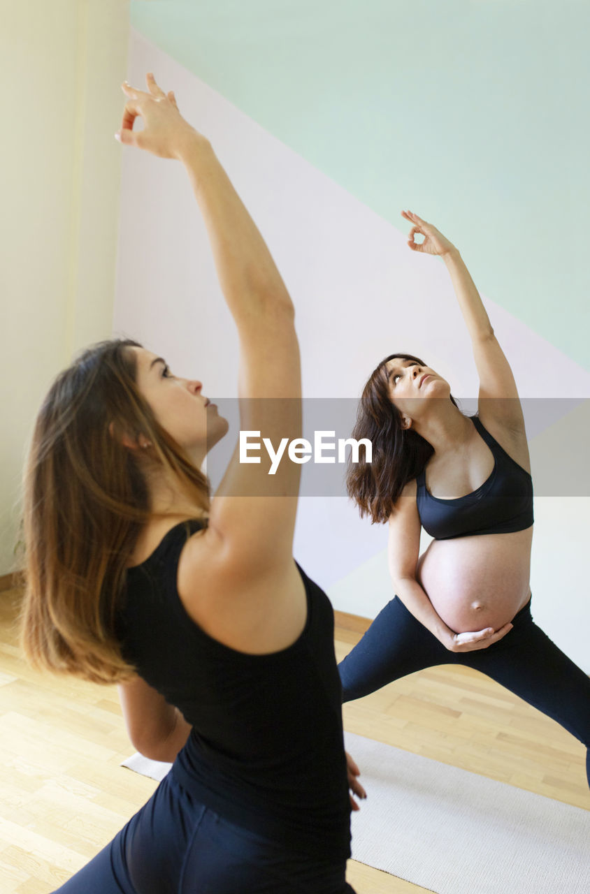 Instructor with hand raised teaching yoga to pregnant woman in studio