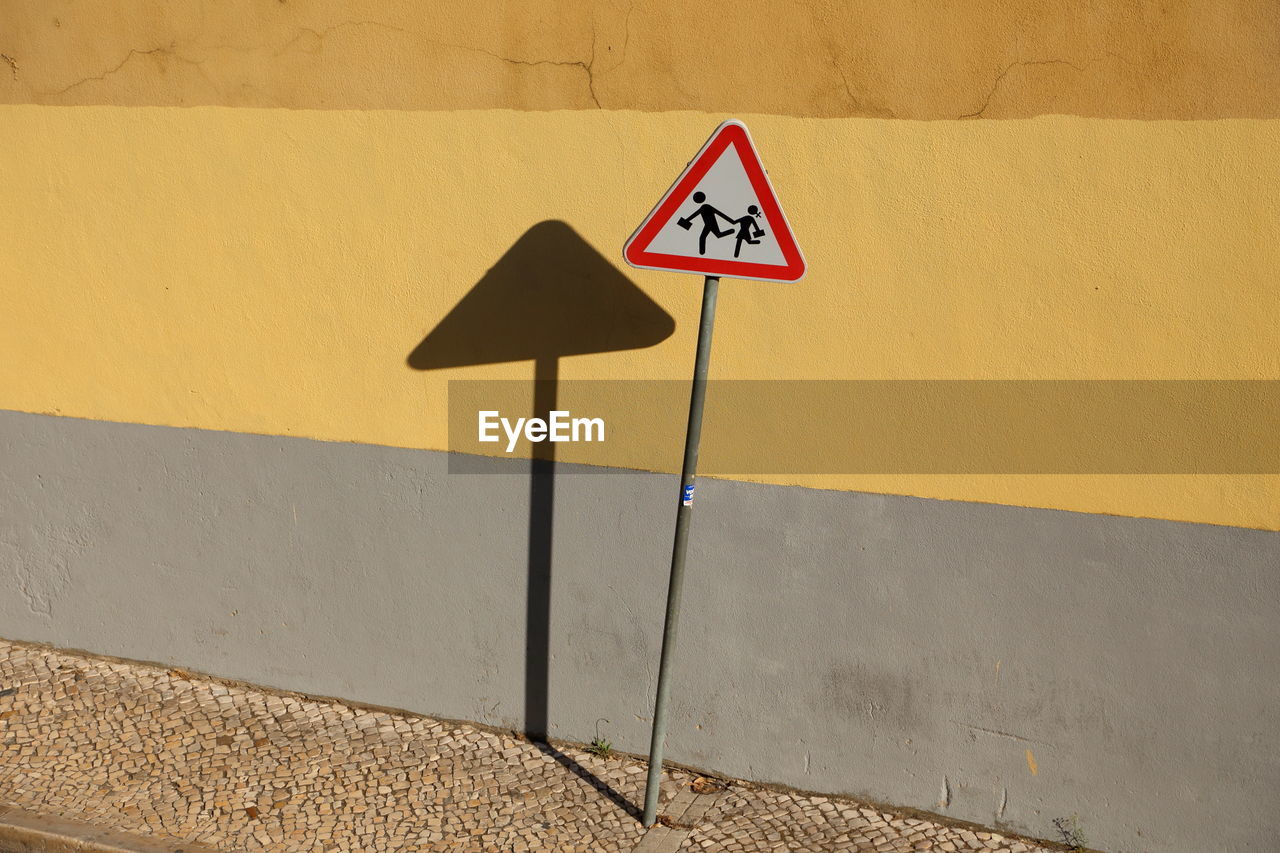 Road sign against wall during sunny day