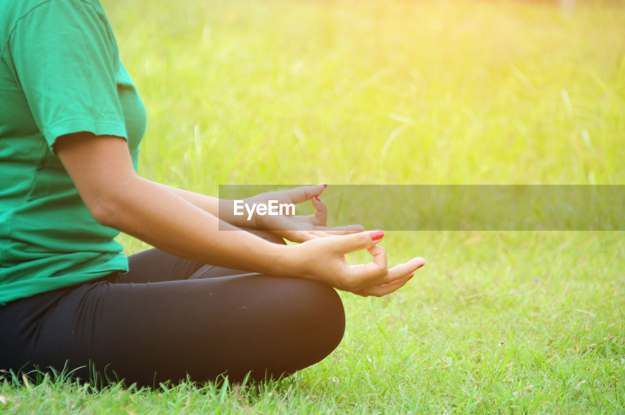Midsection of woman practicing lotus position on grassy field