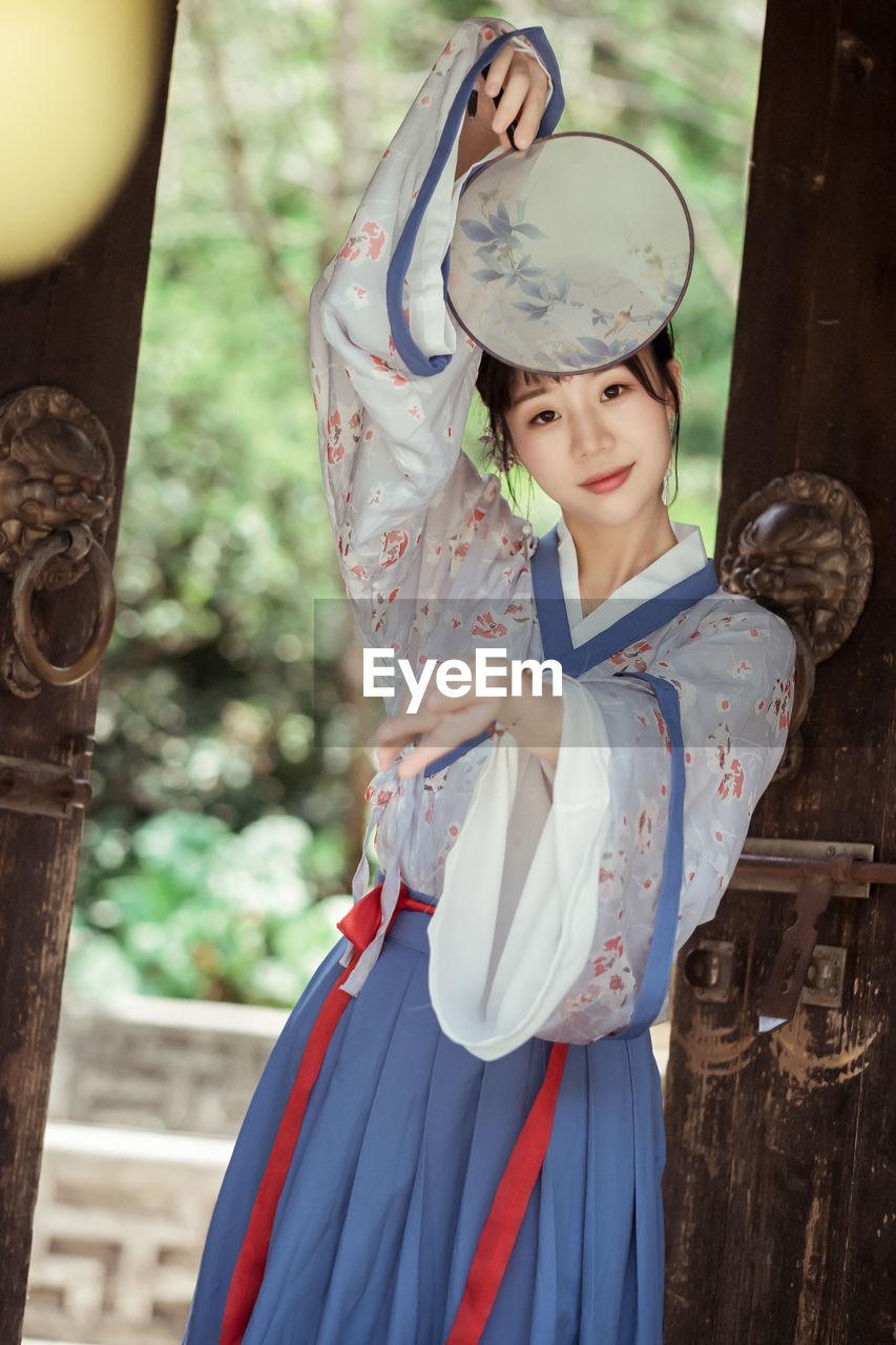 Portrait of woman in kimono holding hand fan at entrance