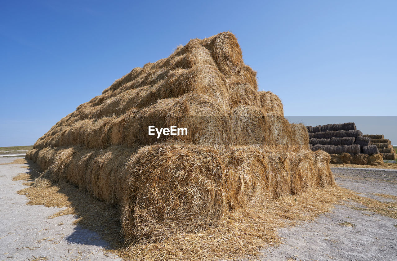 STACK OF HAY BALES ON FIELD AGAINST CLEAR SKY