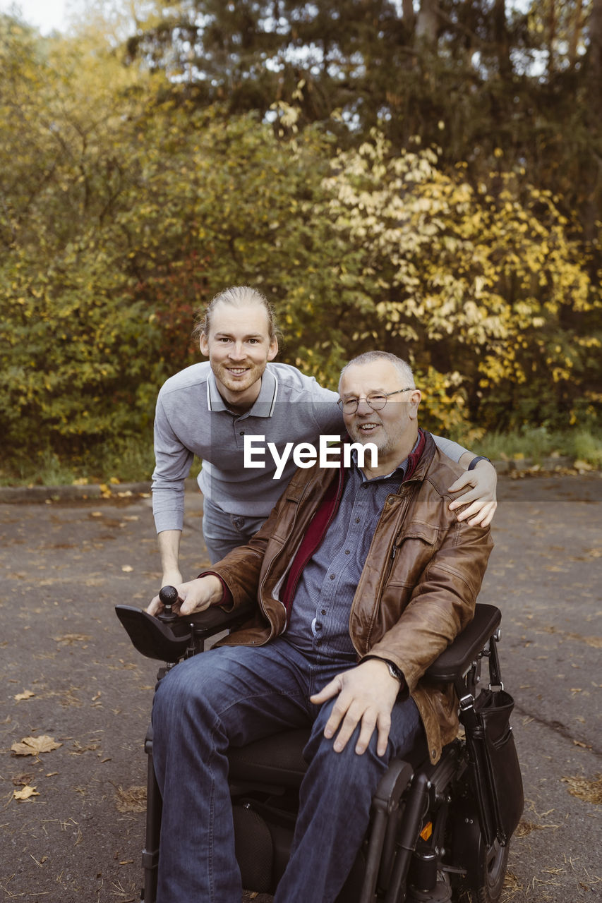 Portrait of smiling young man with arm around father in motorized wheelchair