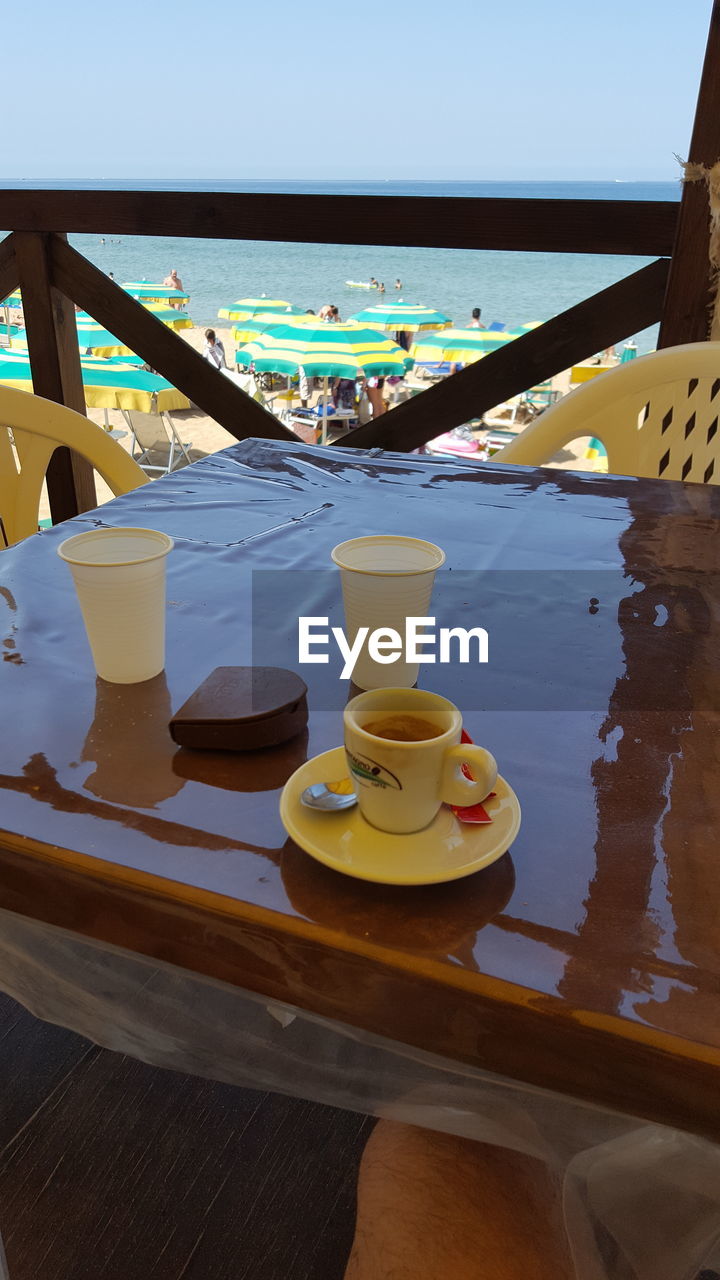 COFFEE CUP ON TABLE AGAINST CLEAR SKY