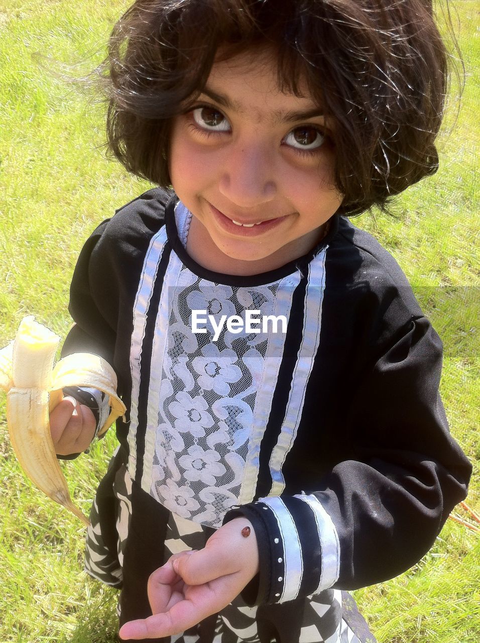 High angle portrait of smiling girl holding banana on grassy field