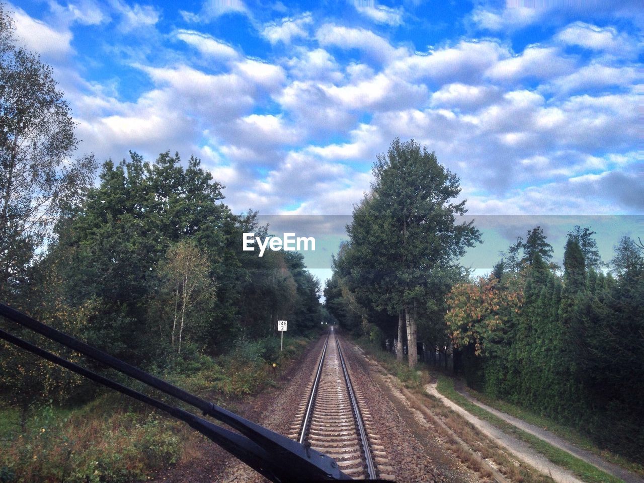 Railroad track amidst trees against cloudy sky