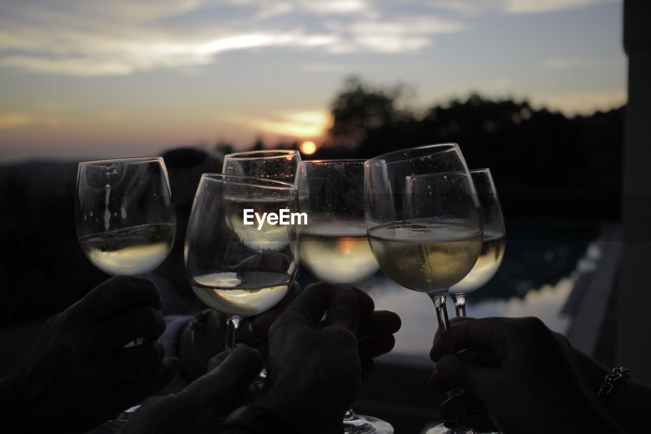 CLOSE-UP OF HAND HOLDING WINE GLASSES AGAINST SUNSET