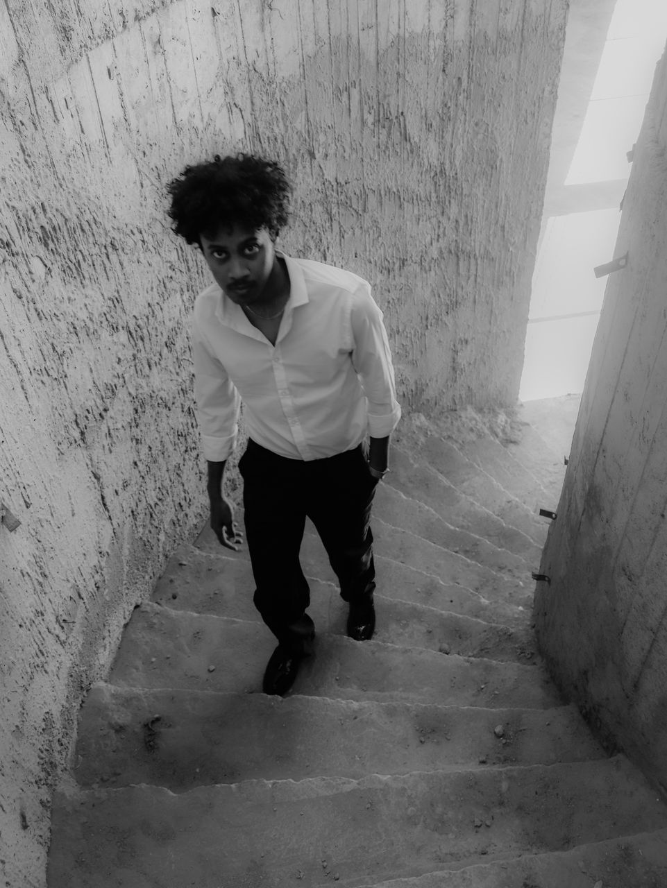 white, black, one person, full length, black and white, architecture, monochrome, monochrome photography, wall - building feature, casual clothing, young adult, lifestyles, adult, snapshot, staircase, leisure activity, men, standing, front view, built structure, day, steps and staircases, footwear, sitting, portrait, outdoors, looking