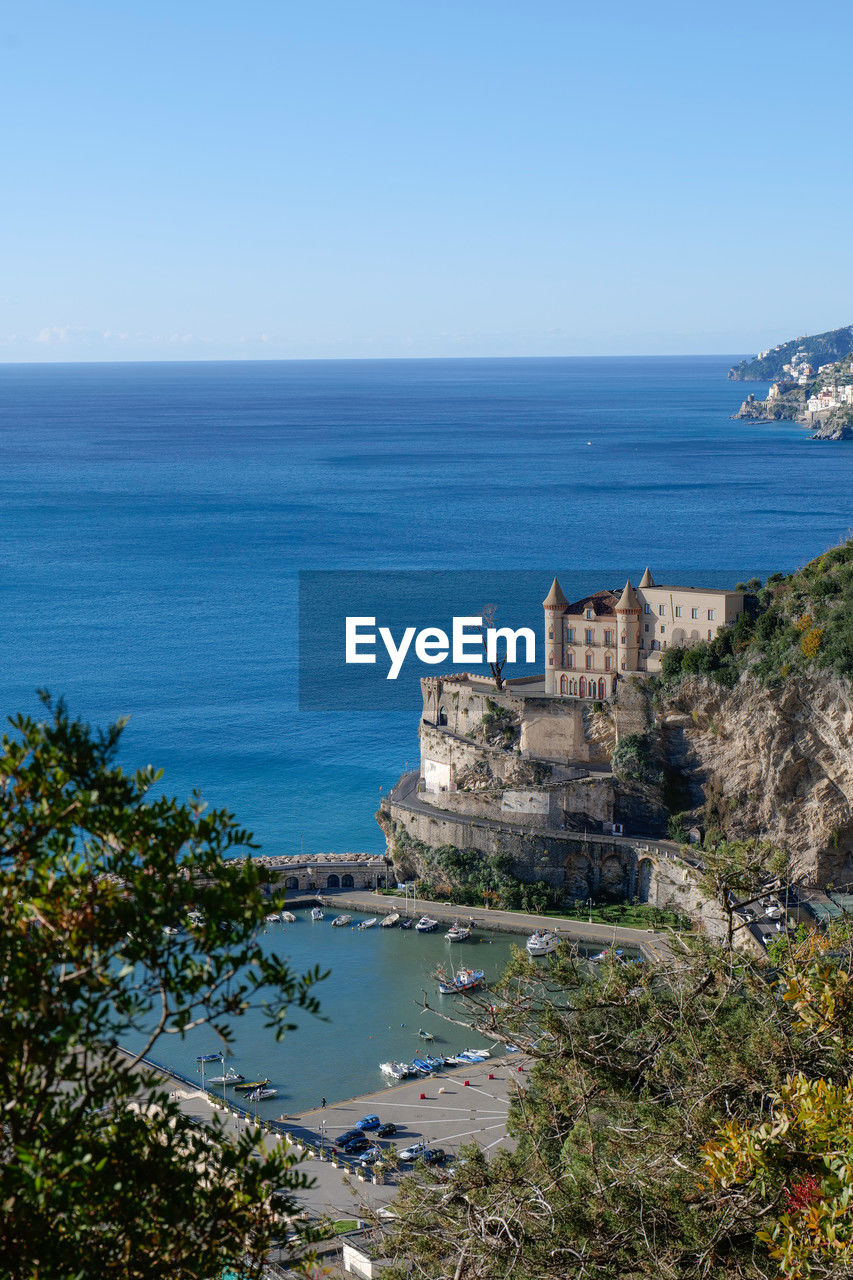 sea, water, coast, sky, land, architecture, horizon over water, nature, vacation, cliff, ocean, scenics - nature, history, travel destinations, built structure, beach, horizon, clear sky, blue, building exterior, shore, the past, travel, tower, beauty in nature, plant, bay, building, no people, tourism, day, terrain, coastline, tree, cove, outdoors, tranquility, body of water, high angle view, fort, promontory, tranquil scene, sunny, ancient, rock, island, mountain, castle, environment, holiday, city, copy space, landscape, islet