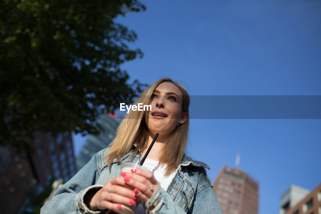 Shocked woman holding disposable cup in city