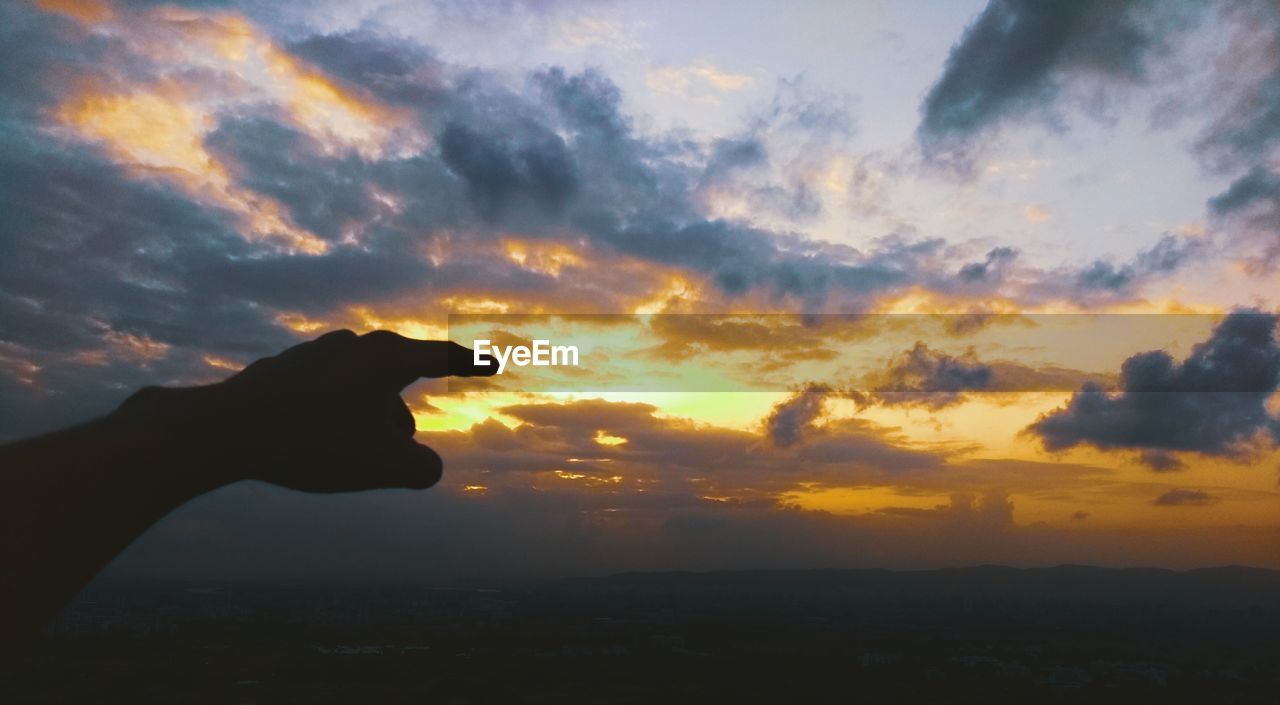 Silhouette hand against sky during sunset