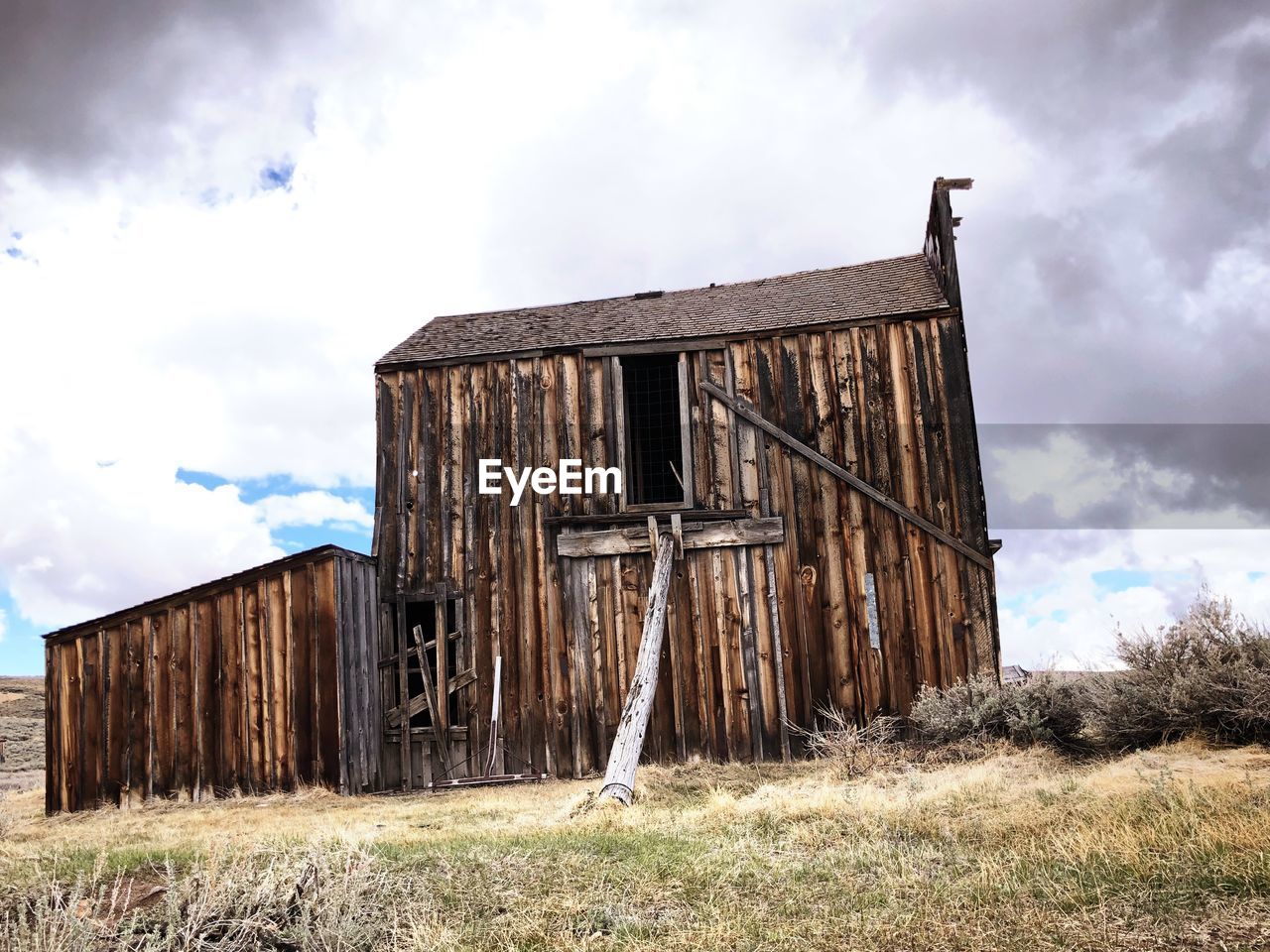 Old abandoned cottages on field against cloudy sky