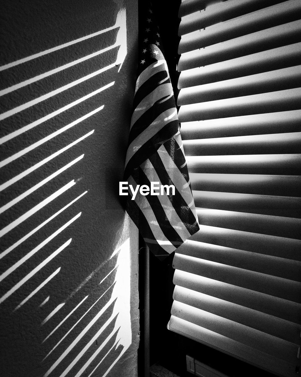 American flag by window blinds, shadows, monochrome image