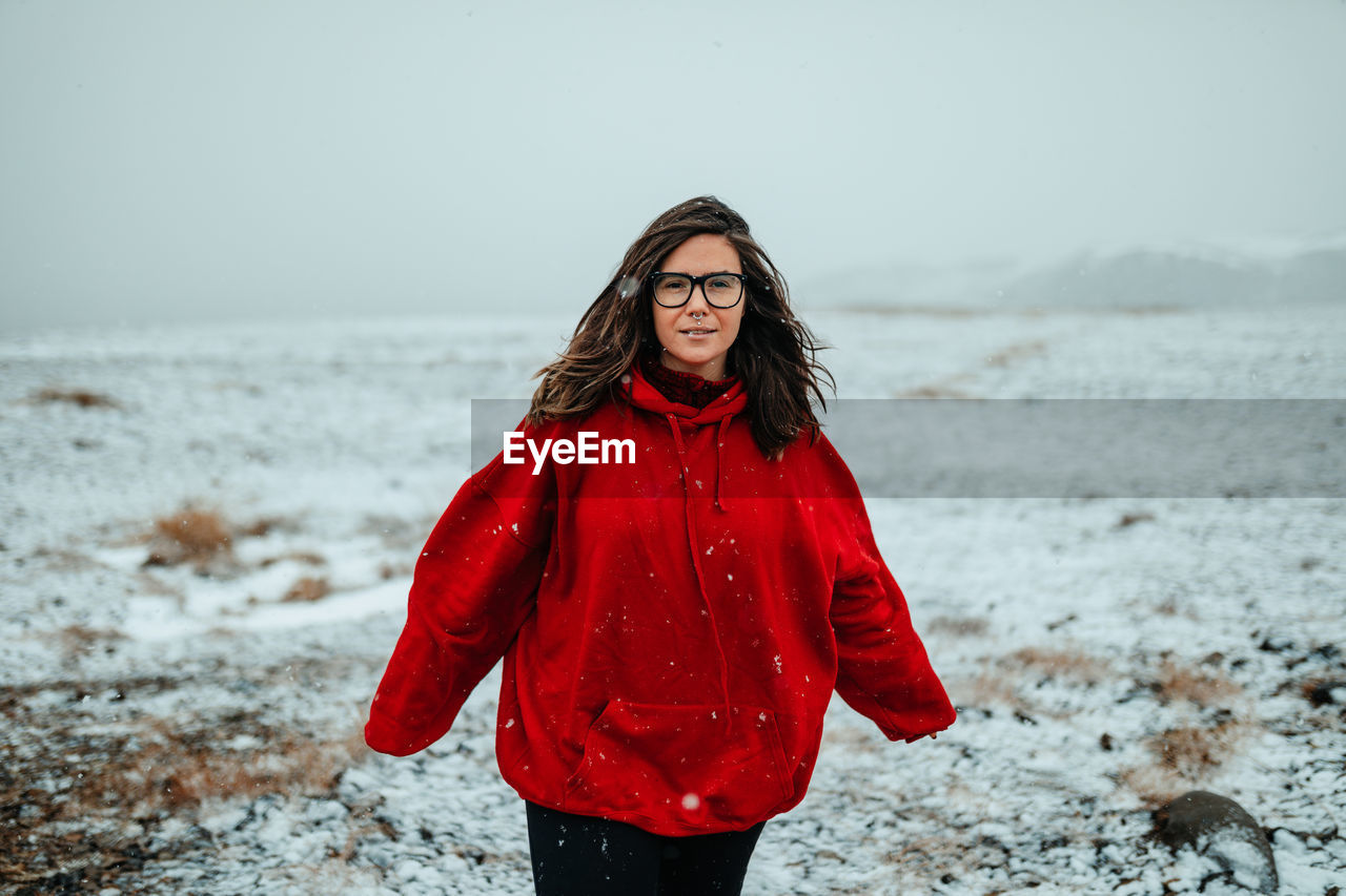 Young happy tourist in eyeglasses with piercing looking at camera between deserted ground in snow