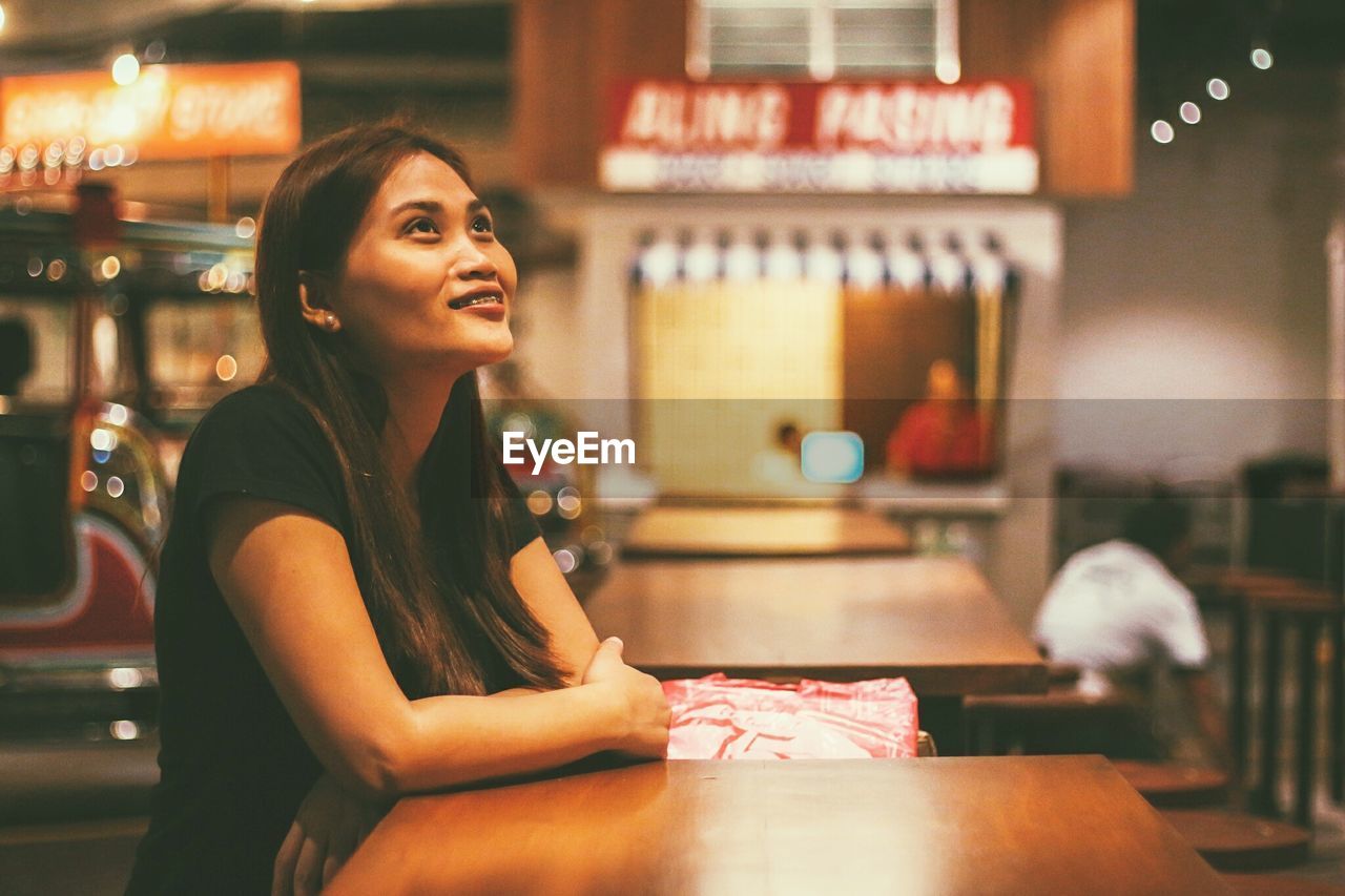 Woman looking away while sitting in illuminated cafe at night