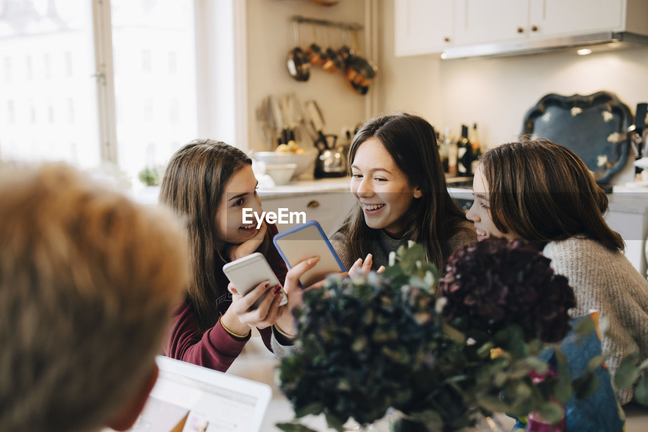 Smiling girls using mobile phone while sitting at table in room