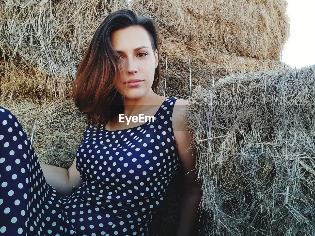 Portrait of young woman relaxing by hay bales on field