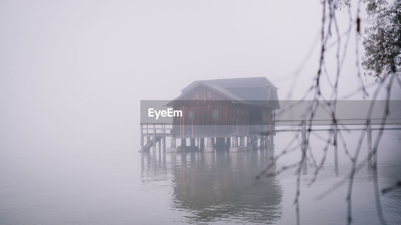 REFLECTION OF HOUSE ON WATER AGAINST SKY IN FOGGY WEATHER