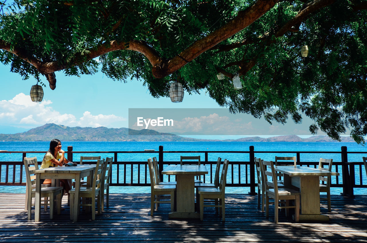 Woman sitting on bench against sea