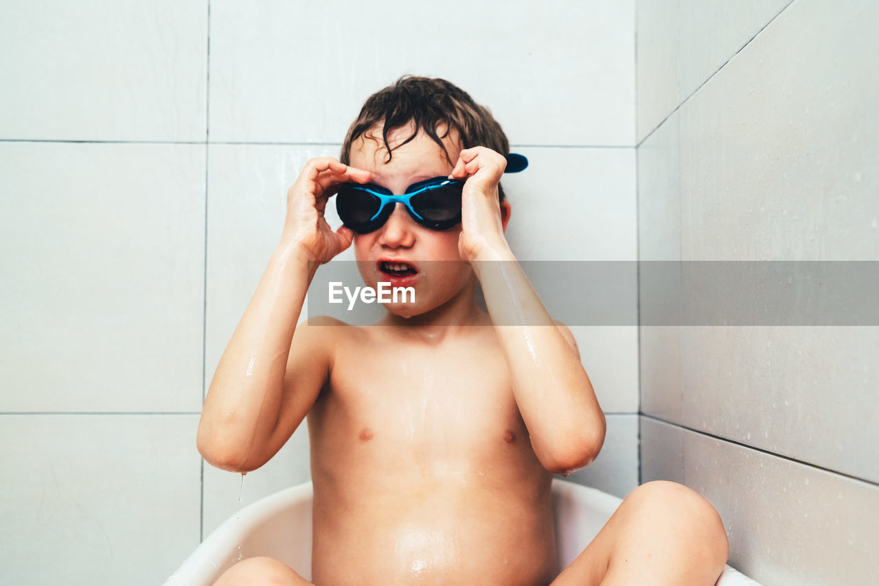 Shirtless boy wearing swimming goggles in bathroom