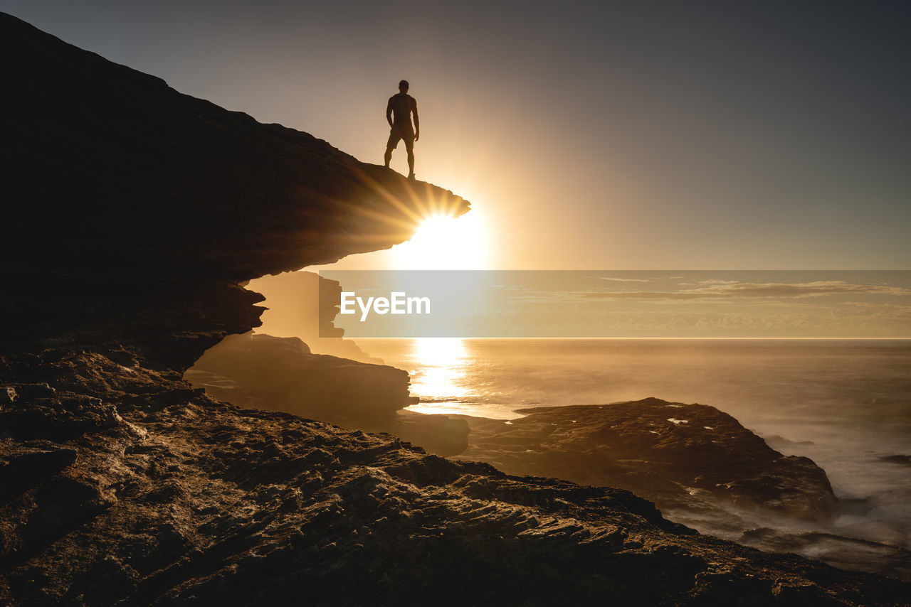 Silhouette of man standing on rock against sky during sunset