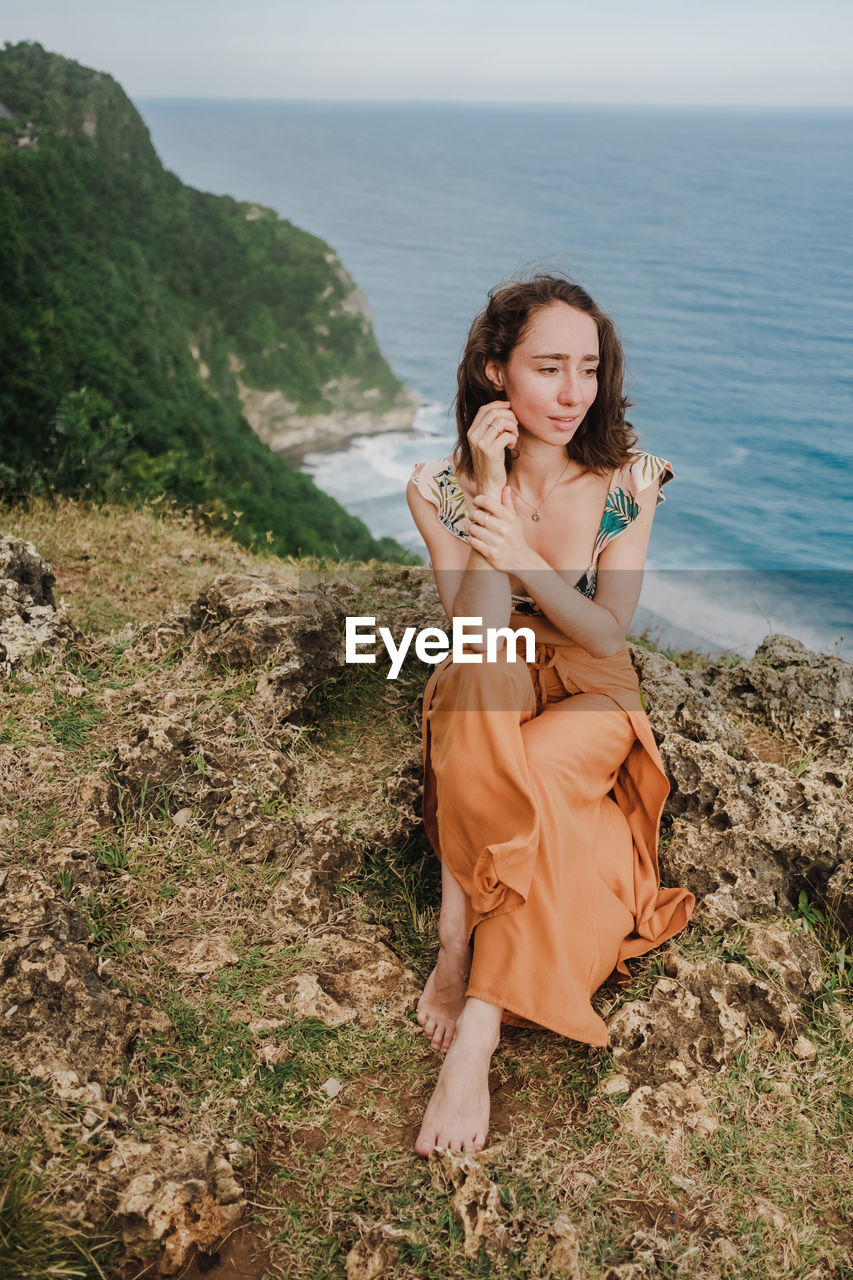 Portrait of beautiful young woman on cliffs edge near ocean.