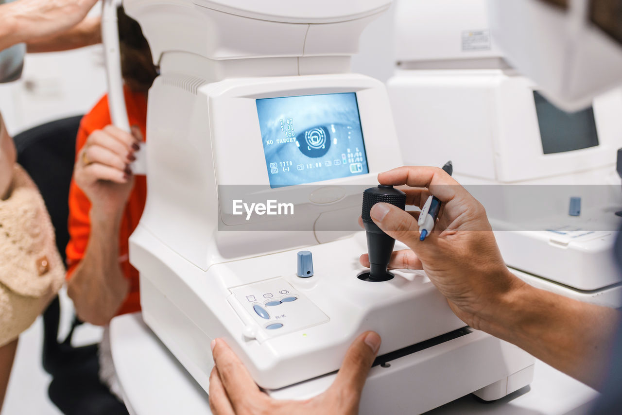 Crop anonymous male doctor ophthalmologist conducting autorefractometry of ocular pressure of female patient on modern equipment of pneumotonometer in ophthalmological clinic