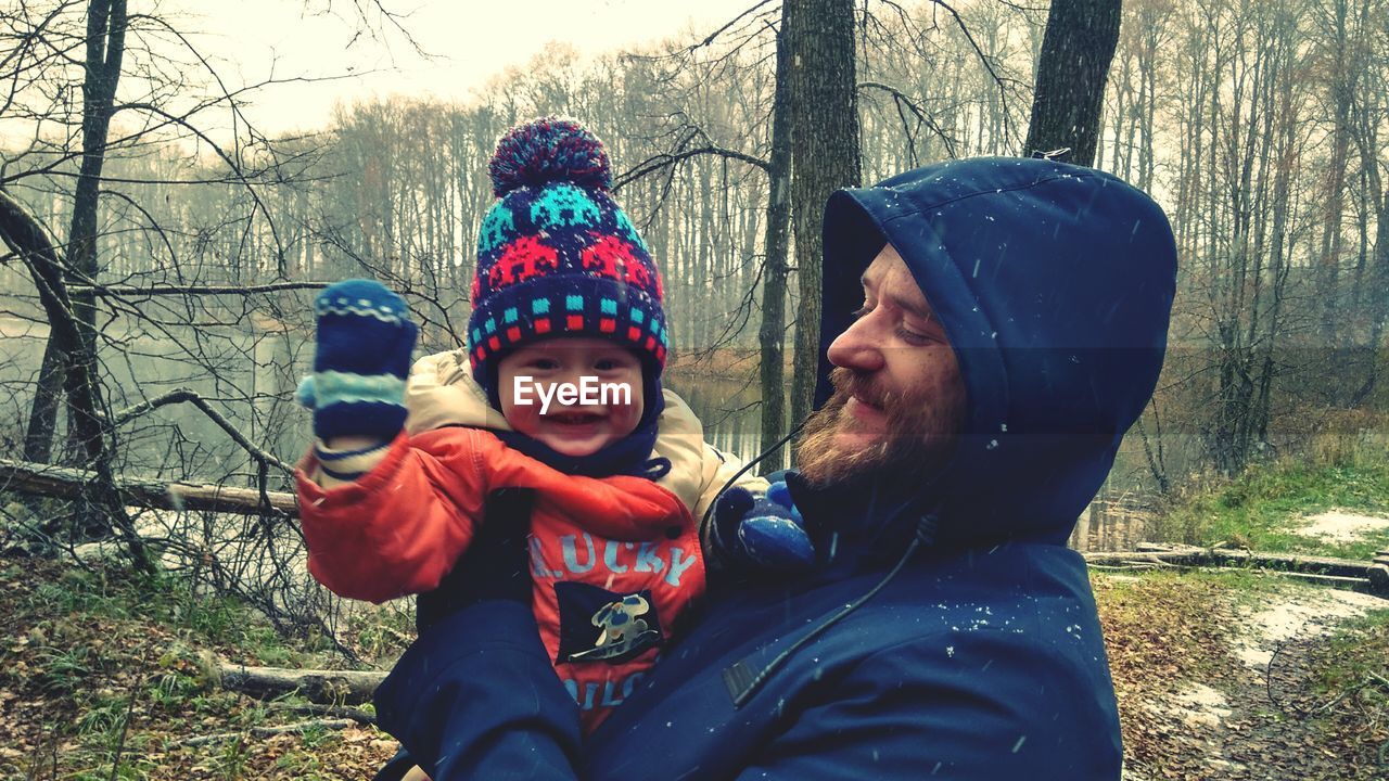 Smiling father and daughter against bare trees during winter